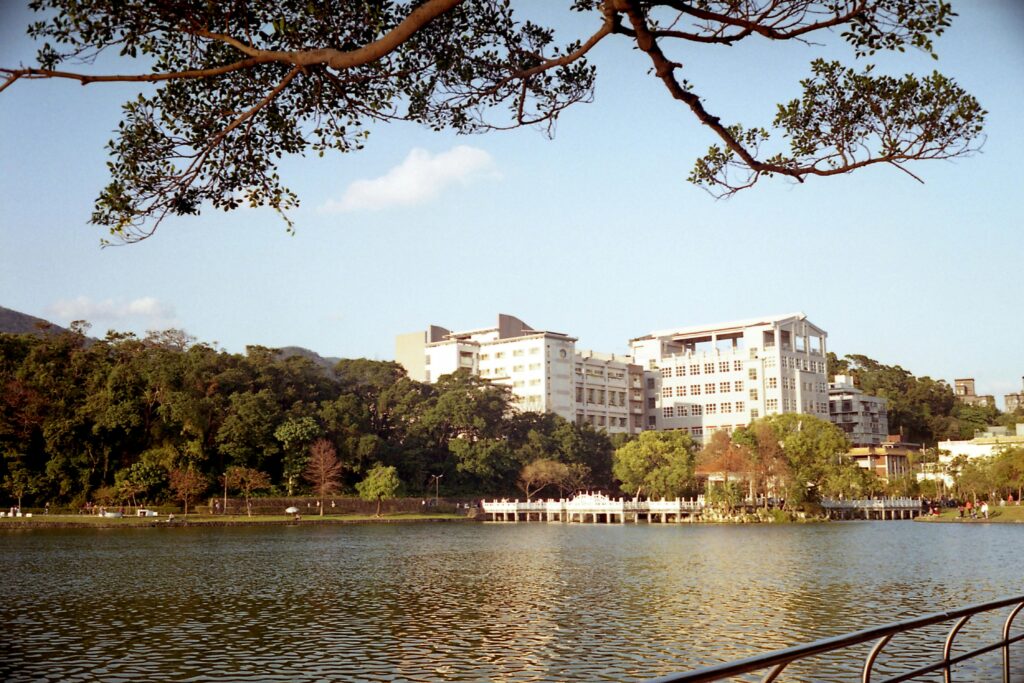 Explore the picturesque riverside campus in Taipei with lush greenery and calm waters under the summer sky.